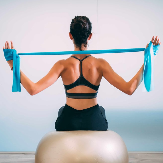 Frau macht Physiotherapie mit Gymnastikball und Terraband