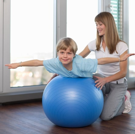 Kind auf Medizinball hat Behandlung bei seiner Physiotherapeutin