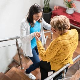 Pflegerin die einer älteren Frau die Treppe herunterhilft
